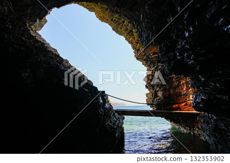 Vertical view of a natural arch in a coastal rock in Budva, Montenegro, with a footbridge passing through it. Scenic Adriatic Sea visible on both sides. Vertical view of a natural arch in a coastal rock in Budva, Montenegro, with a footbridge passing through it. Scenic Adriatic Sea visible on both sides. 132353902