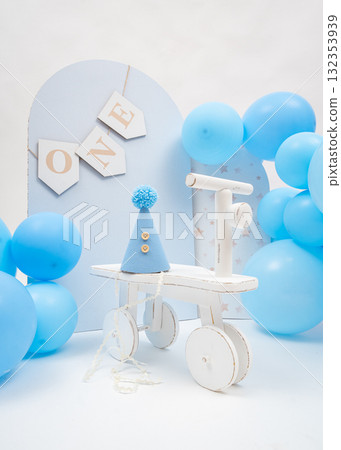 Blue balloons, wooden ONE banner, and small tricycle create soft pastel first birthday setup, perfect for boys milestone celebration 132353939