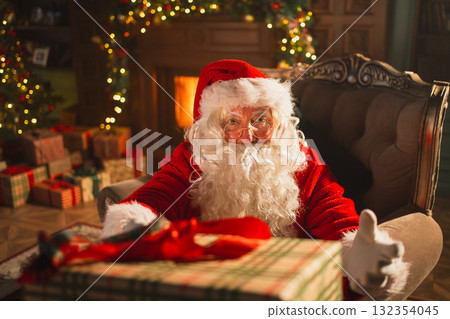 Merry Christmas. Santa Claus giving you present gift box in festive living room with fireplace decorations Christmas tree. Santa packing wrapping gift box on Christmas eve. Winter Holiday Celebrations 132354045