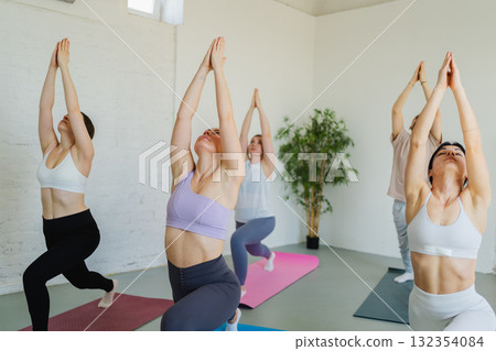 Yoga class Pilates workout. Group of sporty people doing exercise in studio class for yoga wellness mindfulness meditation. Personal trainer men women practicing yoga in gym training stretching indoor 132354084