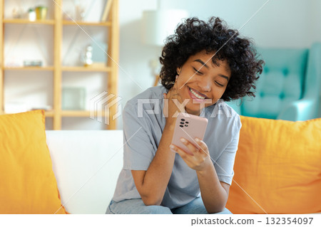 Excited happy young black african american woman holding cell phone laughing feeling joy getting mobile message. Overjoyed girl laughing aloud sitting on couch watching funny video reading news Excited happy young black african american woman holding cell phone laughing feeling joy getting mobile message. Overjoyed girl laughing aloud sitting on couch watching funny video reading news 132354097