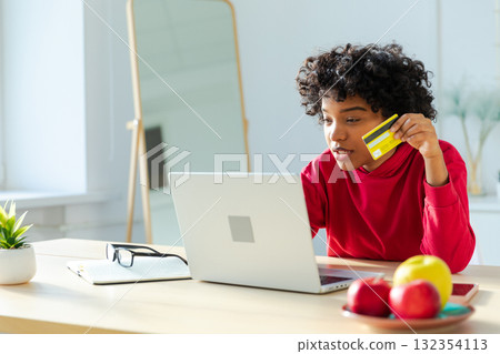 African american woman using laptop shopping online paying with gold credit card. Girl sitting at home buying on Internet enter credit card details. Online shopping ecommerce delivery service African american woman using laptop shopping online paying with gold credit card. Girl sitting at home buying on Internet enter credit card details. Online shopping ecommerce delivery service 132354113