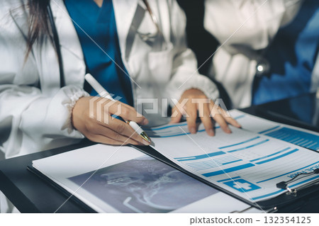 Two doctors and a female nurse meet at a table in the hospital, collaborating on medical tasks using laptops and computers 132354125