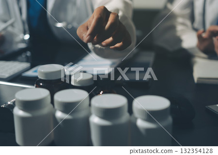 Two doctors and a female nurse meet at a table in the hospital, collaborating on medical tasks using laptops and computers Two doctors and a female nurse meet at a table in the hospital, collaborating on medical tasks using laptops and computers 132354128