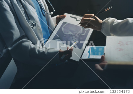 Two doctors and a female nurse meet at a table in the hospital, collaborating on medical tasks using laptops and computers 132354173