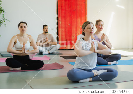 Yoga mindfulness meditation. Group of sporty people doing exercise in studio for class for yoga wellness mindfulness meditation. Men women practicing yoga sitting in lotus pose meditating relaxing 132354234
