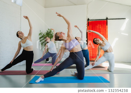Yoga class Pilates workout. Group of sporty people doing exercise in studio class for yoga wellness mindfulness meditation. Personal trainer men women practicing yoga in gym training stretching indoor Yoga class Pilates workout. Group of sporty people doing exercise in studio class for yoga wellness mindfulness meditation. Personal trainer men women practicing yoga in gym training stretching indoor 132354238
