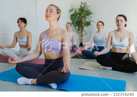 Yoga mindfulness meditation. Group of sporty people doing exercise in studio for class for yoga wellness mindfulness meditation. Men women practicing yoga sitting in lotus pose meditating relaxing 132354240