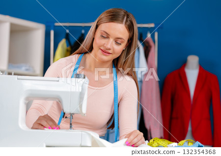 Young seamstress working on her sewing machine on textile factory Young seamstress working on her sewing machine on textile factory 132354368