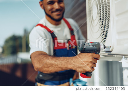 Repairman in uniform installing the outside unit of air conditioner Repairman in uniform installing the outside unit of air conditioner 132354403