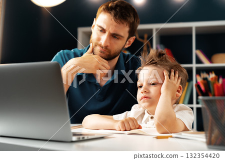 Young boy sitting with his father at the table and using laptop Young boy sitting with his father at the table and using laptop 132354420