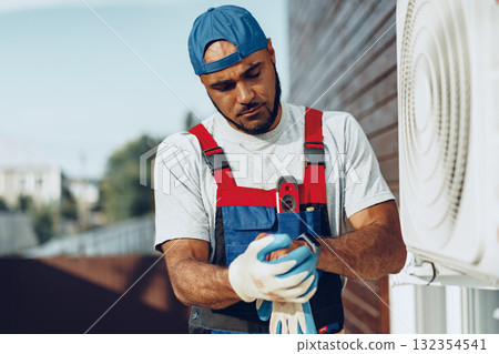 Young black man repairman checking an outside air conditioner unit Young black man repairman checking an outside air conditioner unit 132354541