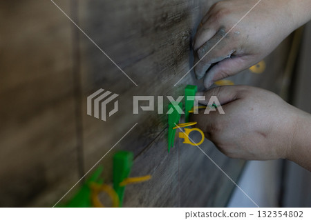 Laying wall tiles. The dirty hands of a worker laying new ceramic tiles on a wall using a leveling system symbolizes home renovation, floor repair, and construction work. Laying wall tiles. The dirty hands of a worker laying new ceramic tiles on a wall using a leveling system symbolizes home renovation, floor repair, and construction work. 132354802