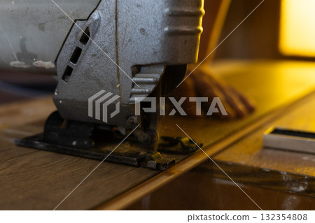 Laying laminate flooring in a house. A man cuts laminate planks with a jigsaw during the installation of new flooring, demonstrating the process of home improvement and DIY renovations. 132354808