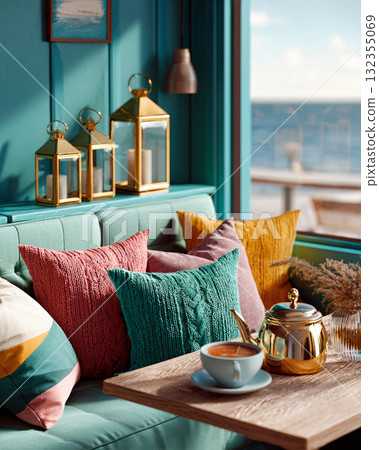 A cozy, well-decorated living area with a view of the ocean through large . The space features teal-colored walls and cushions in shades of green, pink, mustard yellow, peach, and cream. 132355069