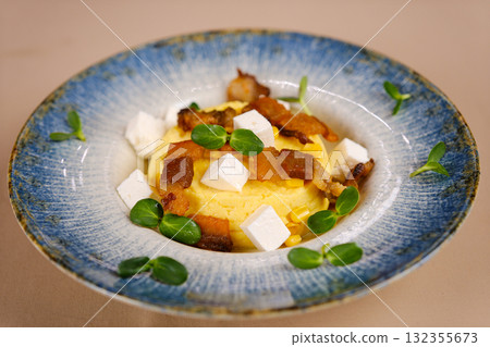 Creamy polenta served with crispy bacon bits, shredded cheese, sun-dried tomato, and fresh herbs in a rustic ceramic bowl. Creamy polenta served with crispy bacon bits, shredded cheese, sun-dried tomato, and fresh herbs in a rustic ceramic bowl. 132355673