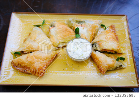 Golden-brown chicken puffs with flaky layers, arranged in a fan shape on a wooden plate, beautifully displayed against a clean white background. 132355693