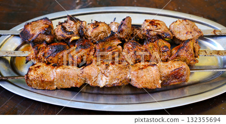 Shashlik or shish kebab prepared on barbecue grill over hot charcoal with grilled vegetables. Grilled pieces of pork meat on metal skewers. 132355694