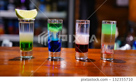 Rainbow drink. Glass shot of alcohol liquor. Bar counter. Rainbow colors. Colored vodka. Rainbow flag, symbol gays and lesbians LGBT, LGBTQ. Good for Party. Rainbow on black background. 132355710