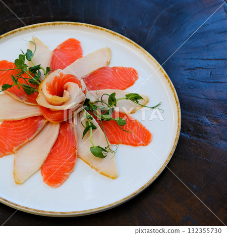 a large plate of sliced salmon and pieces of butterfish. Garnished with herbs and lemon slices. cold appetizer from valuable tasty species of marine fish a large plate of sliced salmon and pieces of butterfish. Garnished with herbs and lemon slices. cold appetizer from valuable tasty species of marine fish 132355730