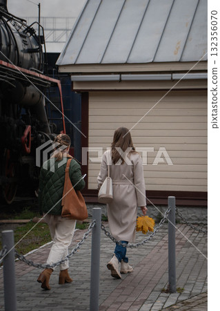 Two women walk near an old steam locomotive at the locomotive museum Povorotny Krug, one holding autumn leaves Two women walk near an old steam locomotive at the locomotive museum Povorotny Krug, one holding autumn leaves 132356070