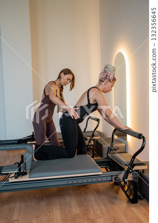 Pilates instructor supports clients, instructor provides supportive guidance for gentle rehabilitation Pilates instructor supports clients, instructor provides supportive guidance for gentle rehabilitation 132356645