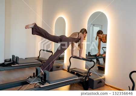 Woman training pilates on the reformer bed. Reformer pilates studio machine for fitness workouts in gym. Fit, healthy and strong authentical body. Fitness concept 132356646