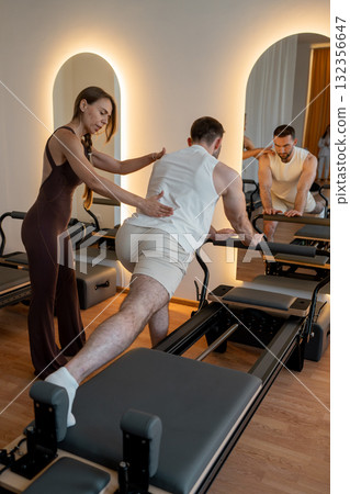 Pilates trainer provides guided support for male client during reformer balance and posture exercises Pilates trainer provides guided support for male client during reformer balance and posture exercises 132356647