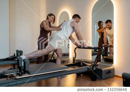 Pilates trainer provides guided support for male client during reformer balance and posture exercises Pilates trainer provides guided support for male client during reformer balance and posture exercises 132356648