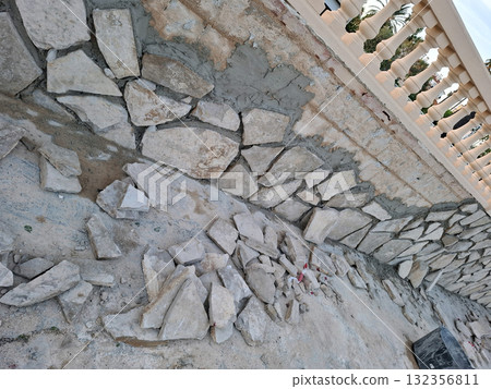 Craftsmen are working on a wall using natural stone pieces of various sizes and shapes. The stones are being arranged unevenly to create a unique finish on the structure. 132356811