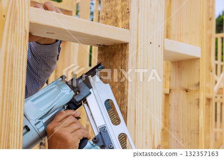 Carpenter is fastening assembly wooden beams in construction site with air nail gun Carpenter is fastening assembly wooden beams in construction site with air nail gun 132357163