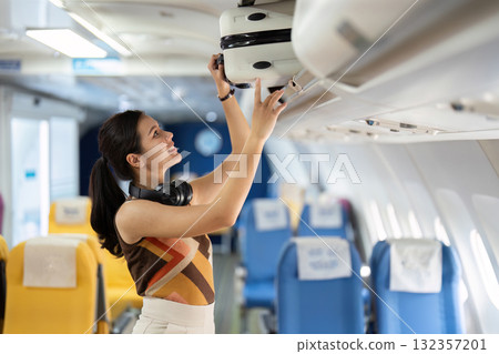 Tourist and Air Travel. A cheerful traveler managing her luggage in the airplane cabin. 132357201