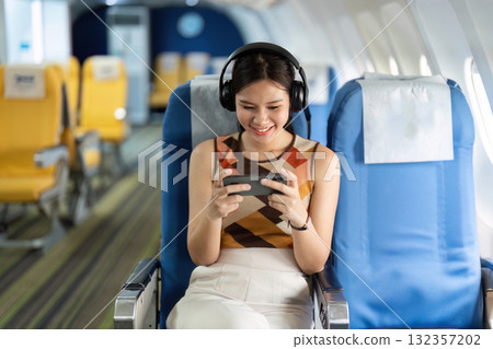 Tourist Enjoying Entertainment on Airplane. A young woman happily watching content on her device. 132357202
