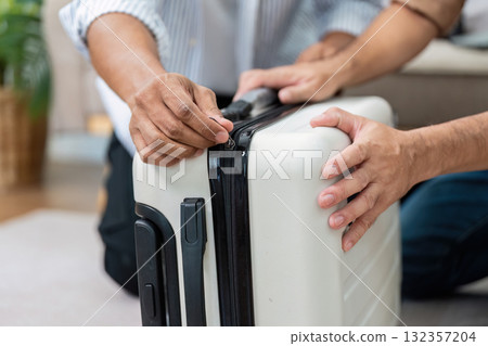Couple Collaborating on Packing. Two partners zip up their suitcase while preparing for a trip. Couple Collaborating on Packing. Two partners zip up their suitcase while preparing for a trip. 132357204