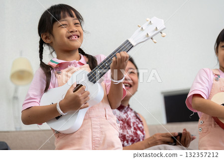 Music and Family Bonding. A young girl joyfully playing a ukulele while her family enjoys a fun moment together. Music and Family Bonding. A young girl joyfully playing a ukulele while her family enjoys a fun moment together. 132357212