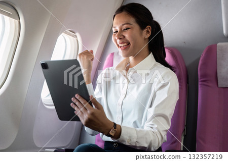 Business travel with a happy professional woman using a tablet while flying Business travel with a happy professional woman using a tablet while flying 132357219
