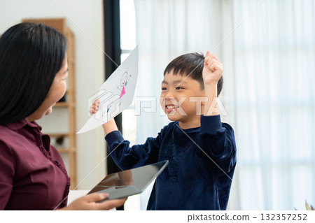 Celebration and Creativity. A young boy proudly shows off his drawing to his mother, capturing a joyful back-to-school moment. Celebration and Creativity. A young boy proudly shows off his drawing to his mother, capturing a joyful back-to-school moment. 132357252