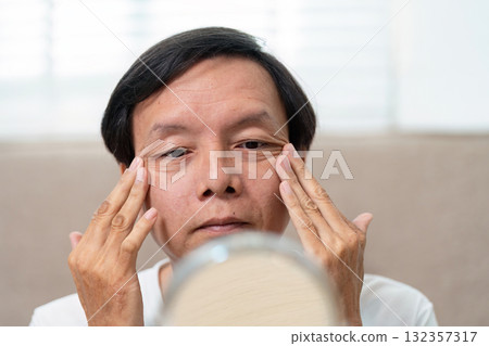 Elderly Facial Care. An elderly man examining his skin in the mirror, focusing on facial health. 132357317