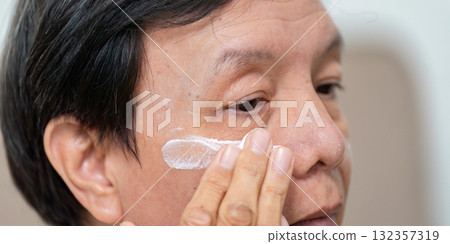 Elderly Skincare Application. An elderly man applying cream to his face with care. Elderly Skincare Application. An elderly man applying cream to his face with care. 132357319