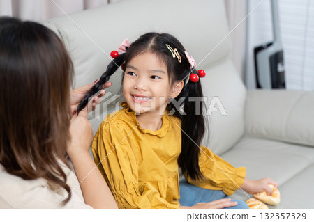 Family Care and Grooming. A mother lovingly styles her daughter's hair in a warm and inviting home setting. 132357329