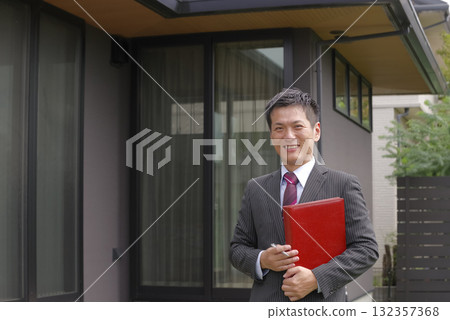 A smiling real estate salesman in front of a newly built house A smiling real estate salesman in front of a newly built house 132357368