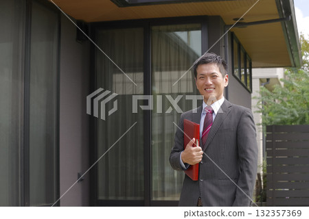 A smiling real estate salesman in front of a newly built house A smiling real estate salesman in front of a newly built house 132357369
