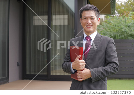 A smiling real estate salesman in front of a newly built house 132357370