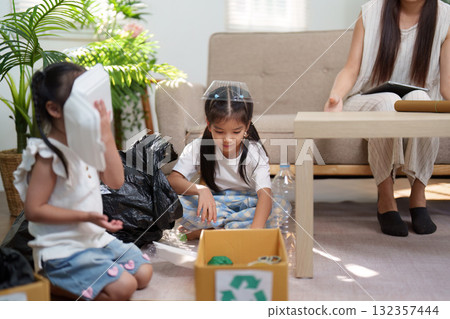 Learning and Play in Sustainability. Young children sort recyclables with their mother, practicing environmental responsibility. 132357444