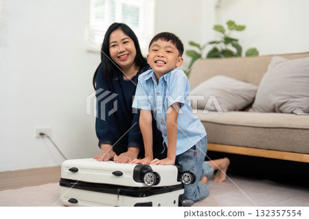 Family Travel Preparation. A mother and son joyfully packing a suitcase together, creating memories before their trip. 132357554