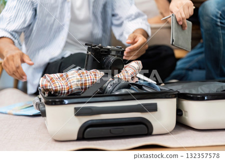 Essentials for a Journey. A couple packing their suitcase with travel items, showcasing their shared excitement and preparation for their trip. 132357578