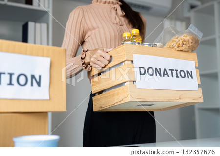 Sustainability and Donation. A woman presents a donation box filled with essential items, showcasing commitment to community support. 132357676