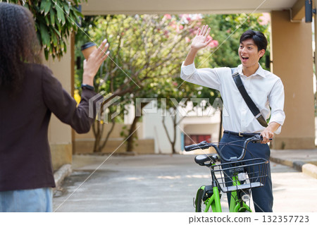 Sustainability and Social Interaction. A young man greets a woman enthusiastically while riding his bicycle in an urban setting. 132357723