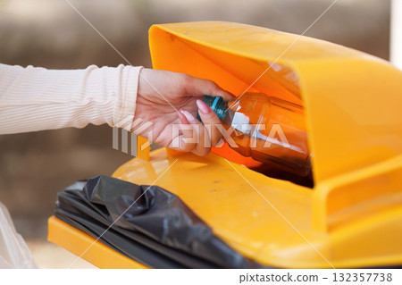Recycling and Waste Management. An individual disposing of a plastic bottle in a recycling bin, contributing to environmental sustainability. Recycling and Waste Management. An individual disposing of a plastic bottle in a recycling bin, contributing to environmental sustainability. 132357738
