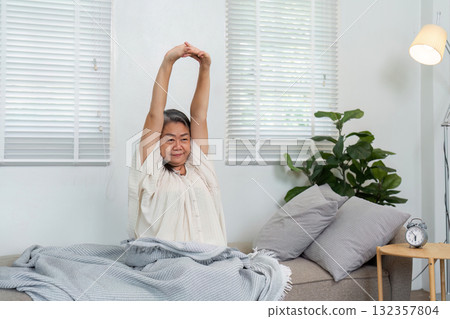Stretching and Wellness. An elderly woman performing morning stretches on a couch, embracing a healthy lifestyle. Stretching and Wellness. An elderly woman performing morning stretches on a couch, embracing a healthy lifestyle. 132357804